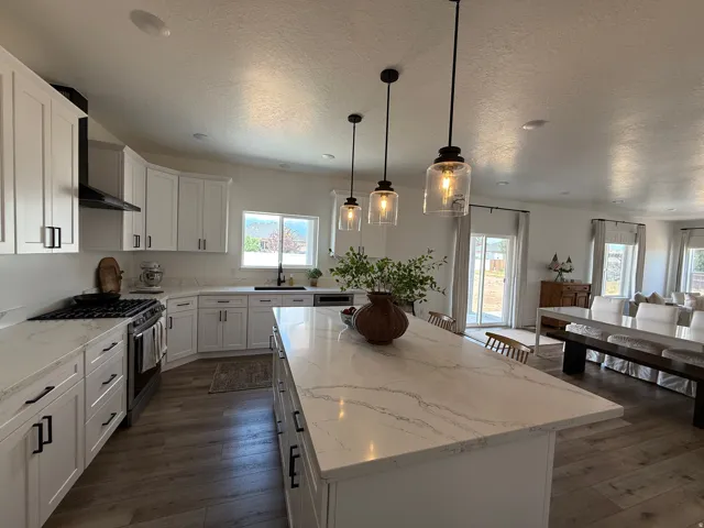 Open-concept kitchen featuring an expansive island with a waterfall countertop, contemporary pendant lighting, white shaker cabinetry, and wood-finish flooring