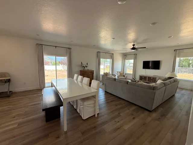 Open-concept living area featuring wood-finish flooring, white walls, recessed lighting, a ceiling fan, and multiple windows with roller shades