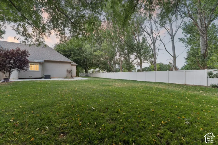 Expansive green lawn featuring a full privacy fence, mature trees, and a concrete patio