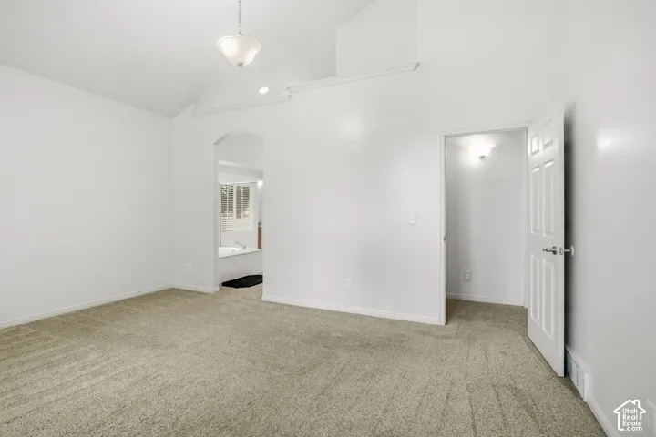 Carpeted room featuring a vaulted ceiling with a semi-flush mount light fixture and an arched doorway leading to a bath area with a built-in tub