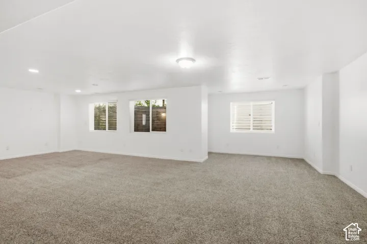 Spacious room featuring neutral carpeting, recessed lighting, white walls, and multiple windows providing natural light