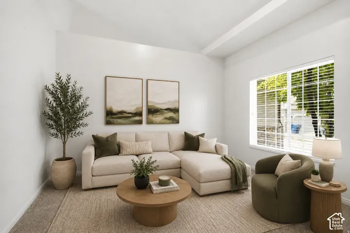 Vaulted ceiling with exposed beam, large window with blinds, light-toned wall finishes, and carpeted flooring