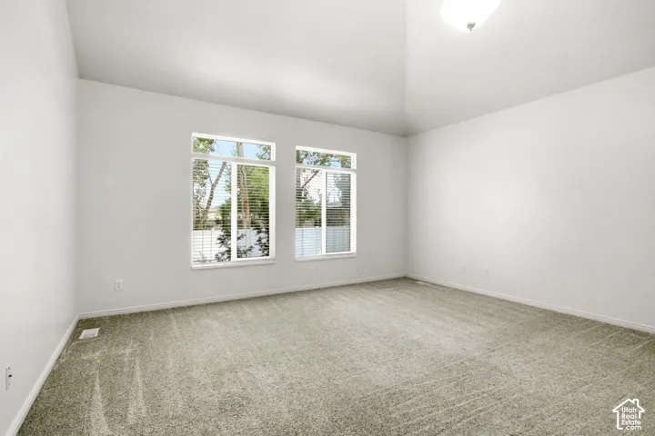 Spacious room featuring vaulted ceilings, light gray carpeting, and two large window units with blinds