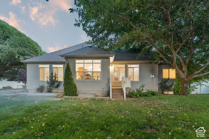 Rear exterior featuring a large grassy area, mature trees, multi-pane windows, and a raised exterior staircase