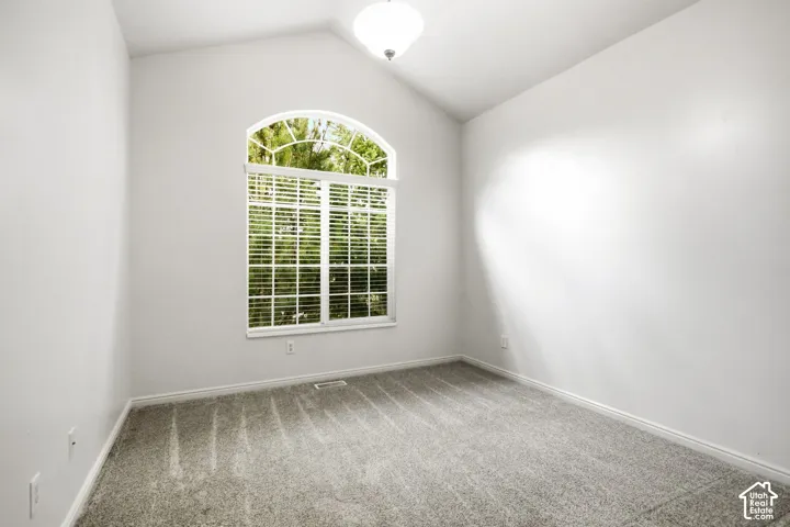 Room featuring a vaulted ceiling, arched top window with white blinds, neutral carpeting, and a flush-mount ceiling light fixture