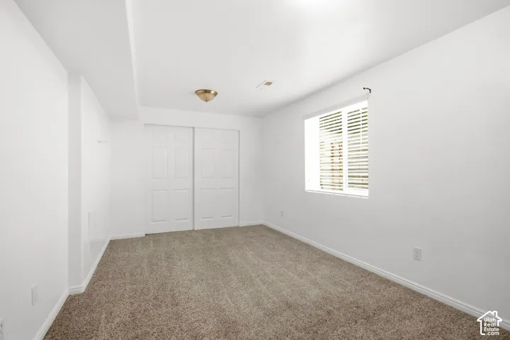 Carpeted room featuring a window with blinds, white walls, and a ceiling-mounted light fixture