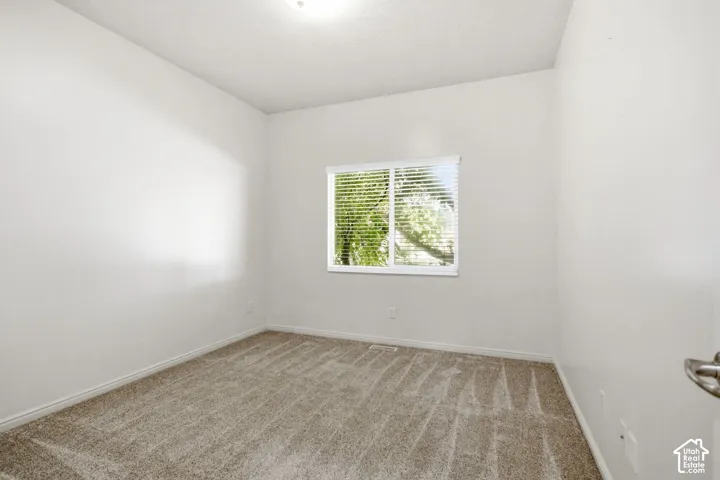 Carpeted room featuring a single window with horizontal blinds, white walls, and a ceiling-mounted light fixture