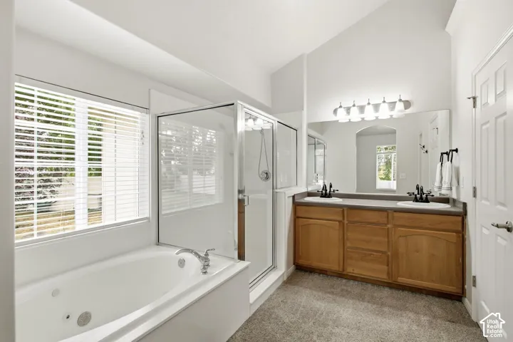 Bathroom featuring a jetted soaking tub, glass-enclosed shower, dual vanity with wood cabinetry, and vaulted ceilings