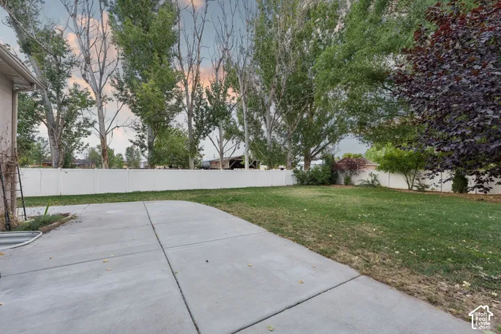 Expansive lawn area featuring a white privacy fence, mature trees, concrete patio space, and varied landscaping