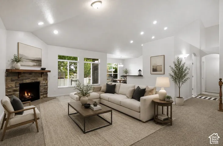 Bright and spacious living room featuring recessed ceiling lighting, a gas fireplace with stone surround, large multi-pane windows with natural light, neutral wood-finish flooring, and neutral upholstered seating areas anchored by a low-profile metal-fram