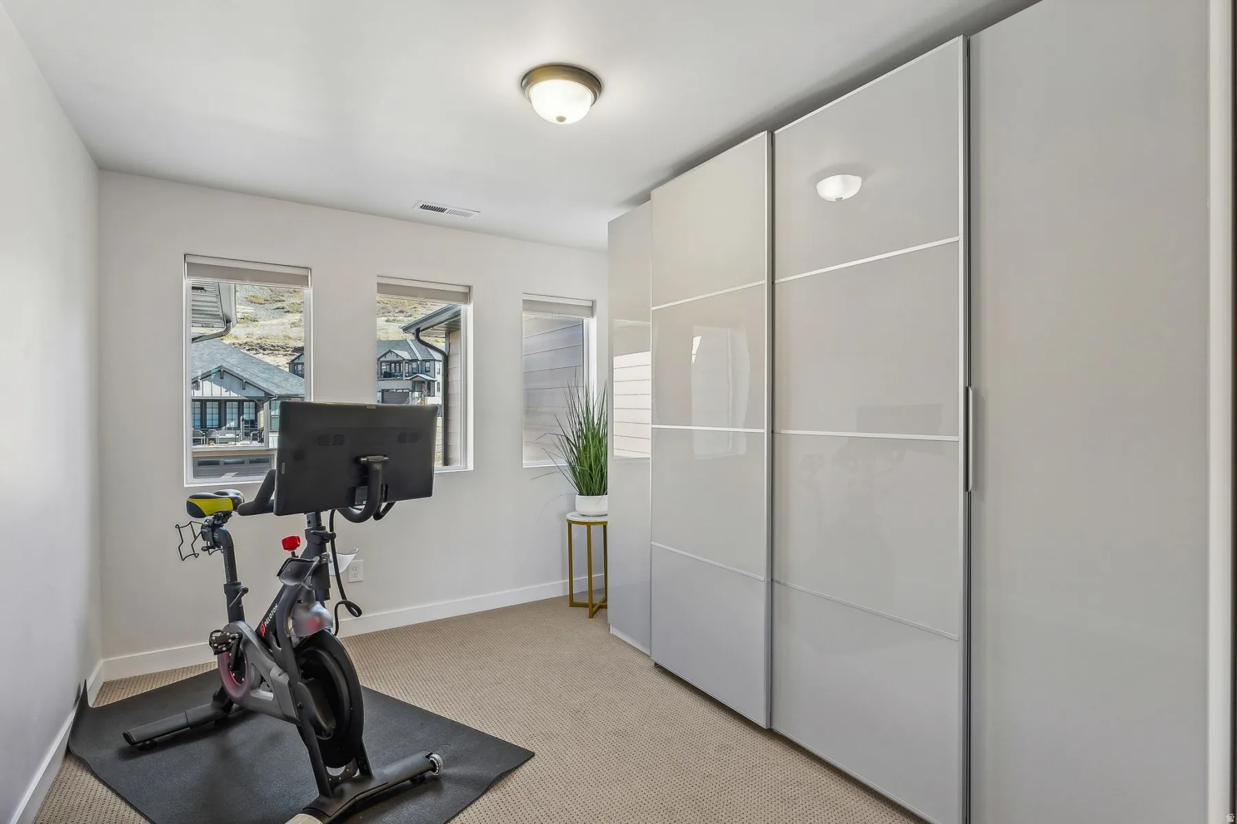Recessed lighting illuminates a room featuring three windows with roller shades, neutral carpeting, and a built-in wardrobe with glossy panel doors and integrated handles