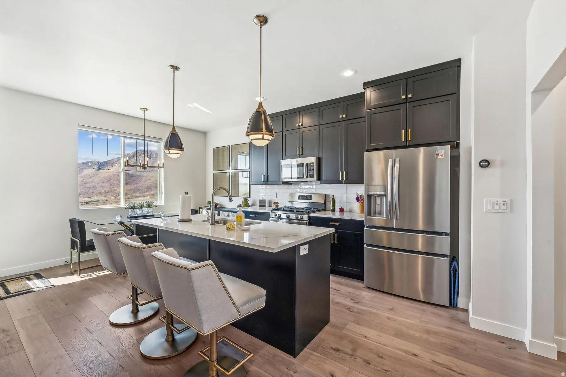 Open-concept kitchen featuring dark cabinetry, stainless steel appliances, a white subway tile backsplash, and a central island with countertop seating