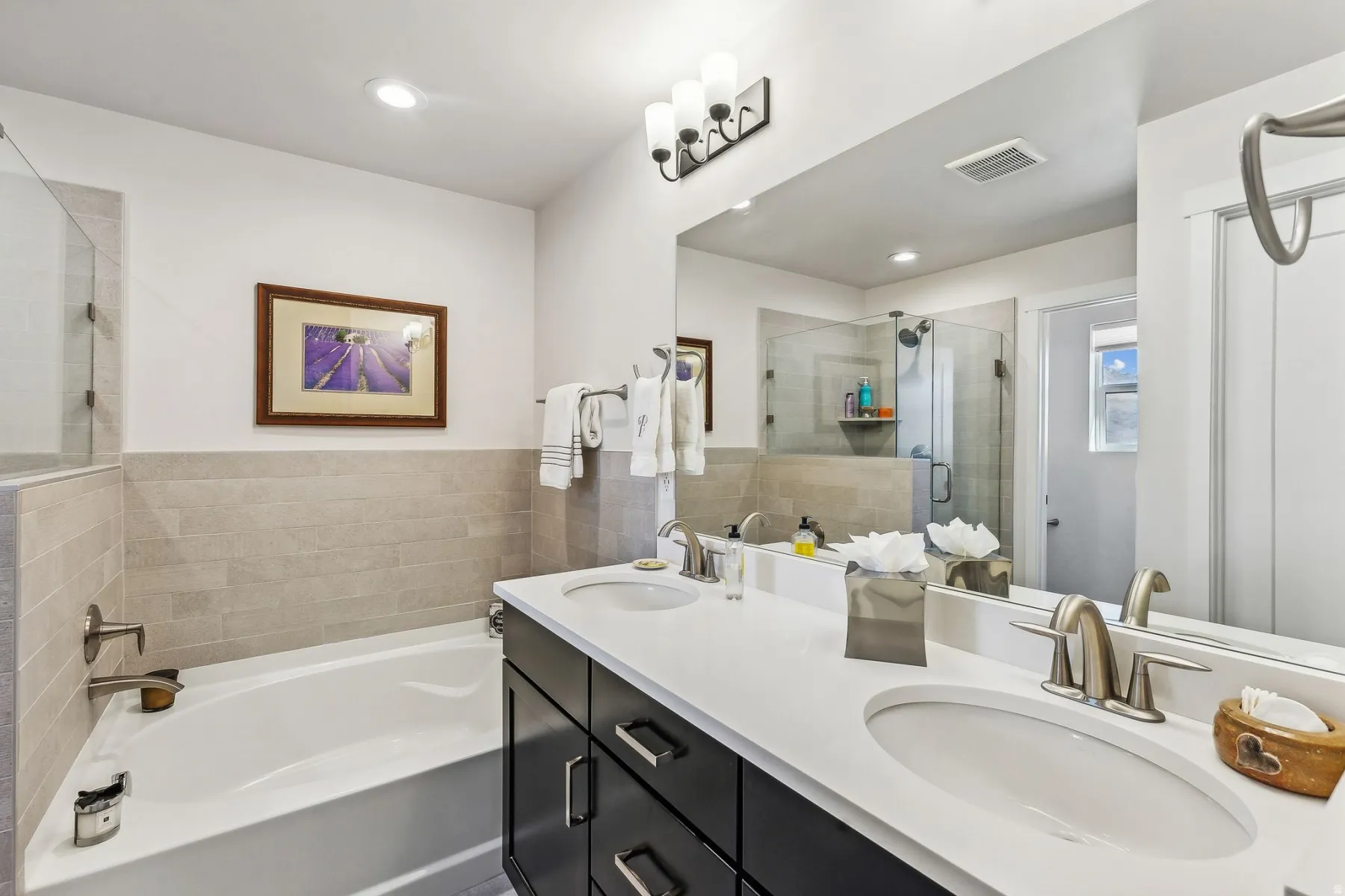 Bathroom featuring a double vanity with undermount sinks, a bathtub with a tiled surround, a glass-enclosed shower, and brushed nickel fixtures