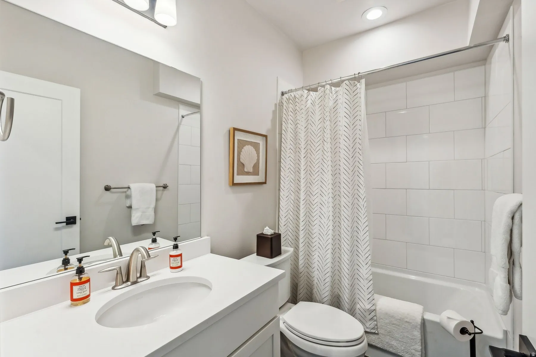 Bathroom featuring a white vanity with an integrated sink, brushed nickel faucet, large wall mirror, and a tiled tub/shower combination