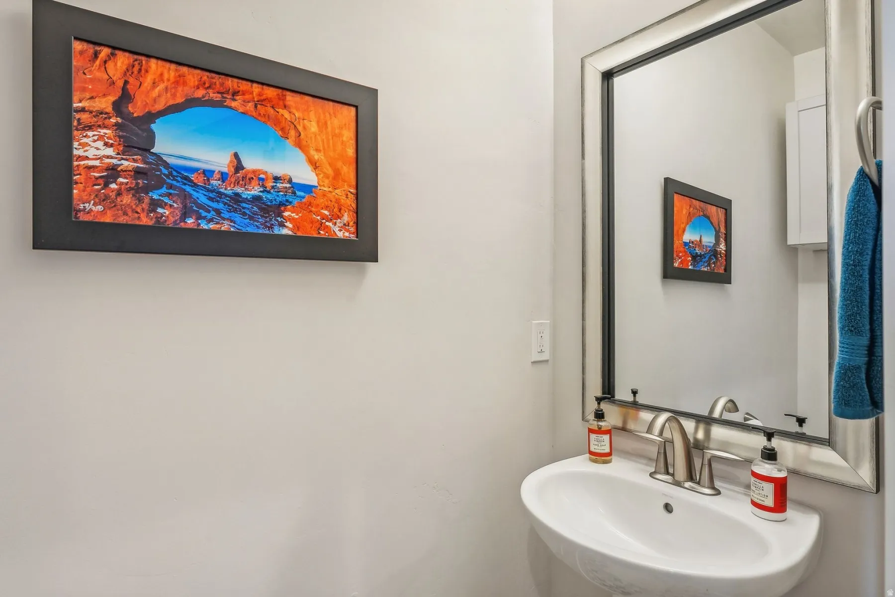 Pedestal sink with brushed nickel faucet, framed mirror, and light gray wall paint