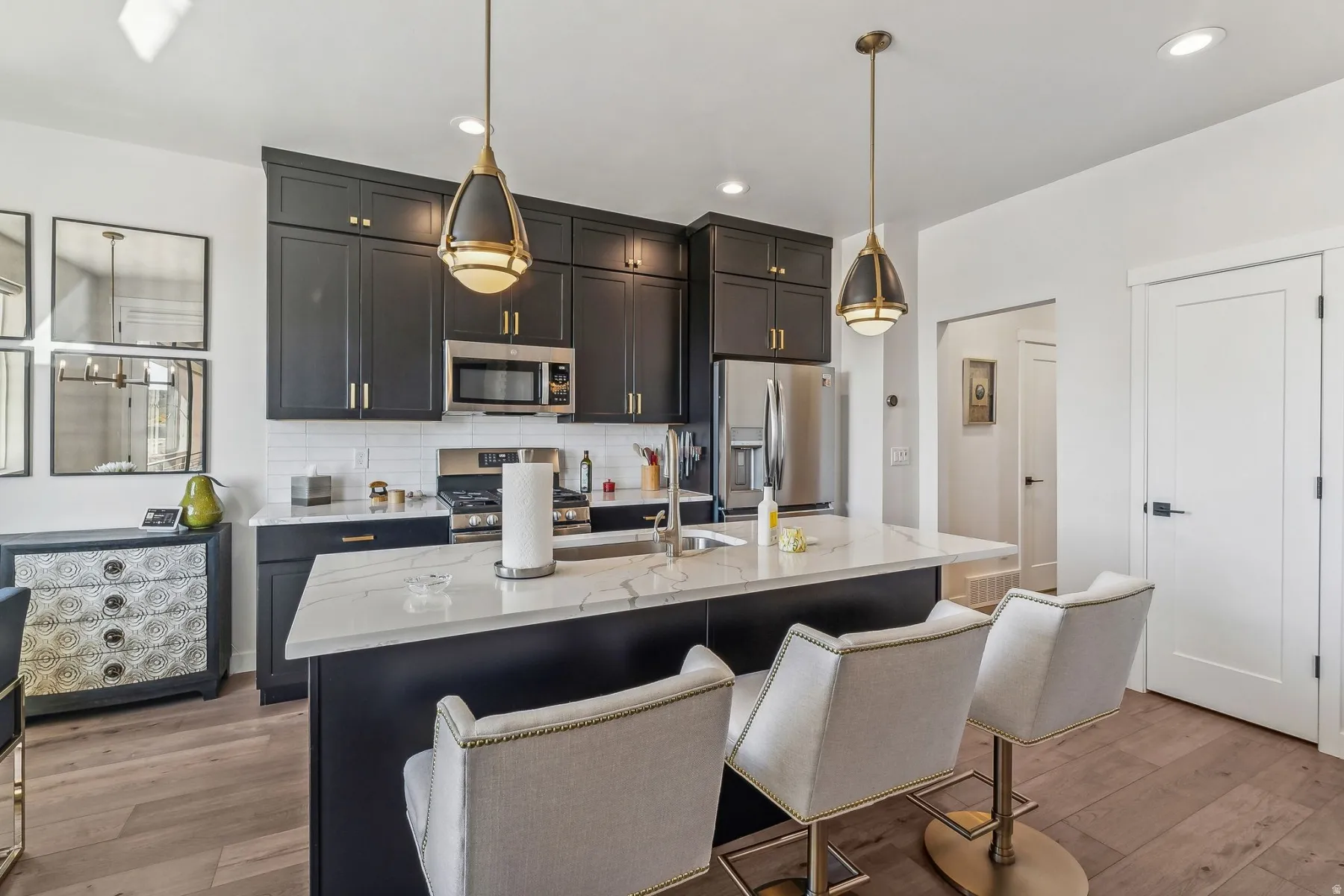Kitchen featuring dark cabinetry, stainless steel appliances, white subway tile backsplash, a large island with a light-colored countertop, and wood-finish flooring