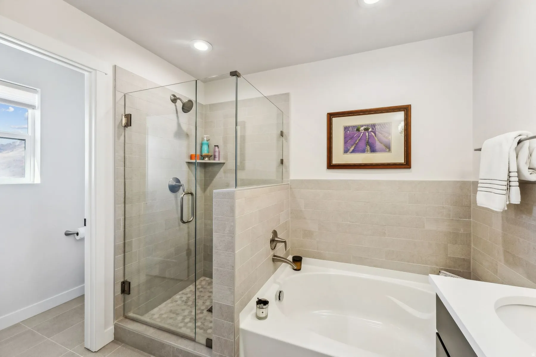 White bathroom featuring a glass-enclosed shower with pebble-tile flooring and a built-in niche, a soaking tub, and neutral tiled walls