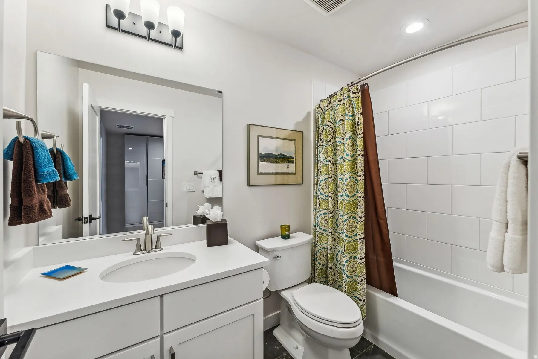 Bathroom featuring a built-in vanity with an undermount sink, a large wall-mounted mirror, brushed nickel fixtures, a white tiled shower/tub combination, and dark tile flooring