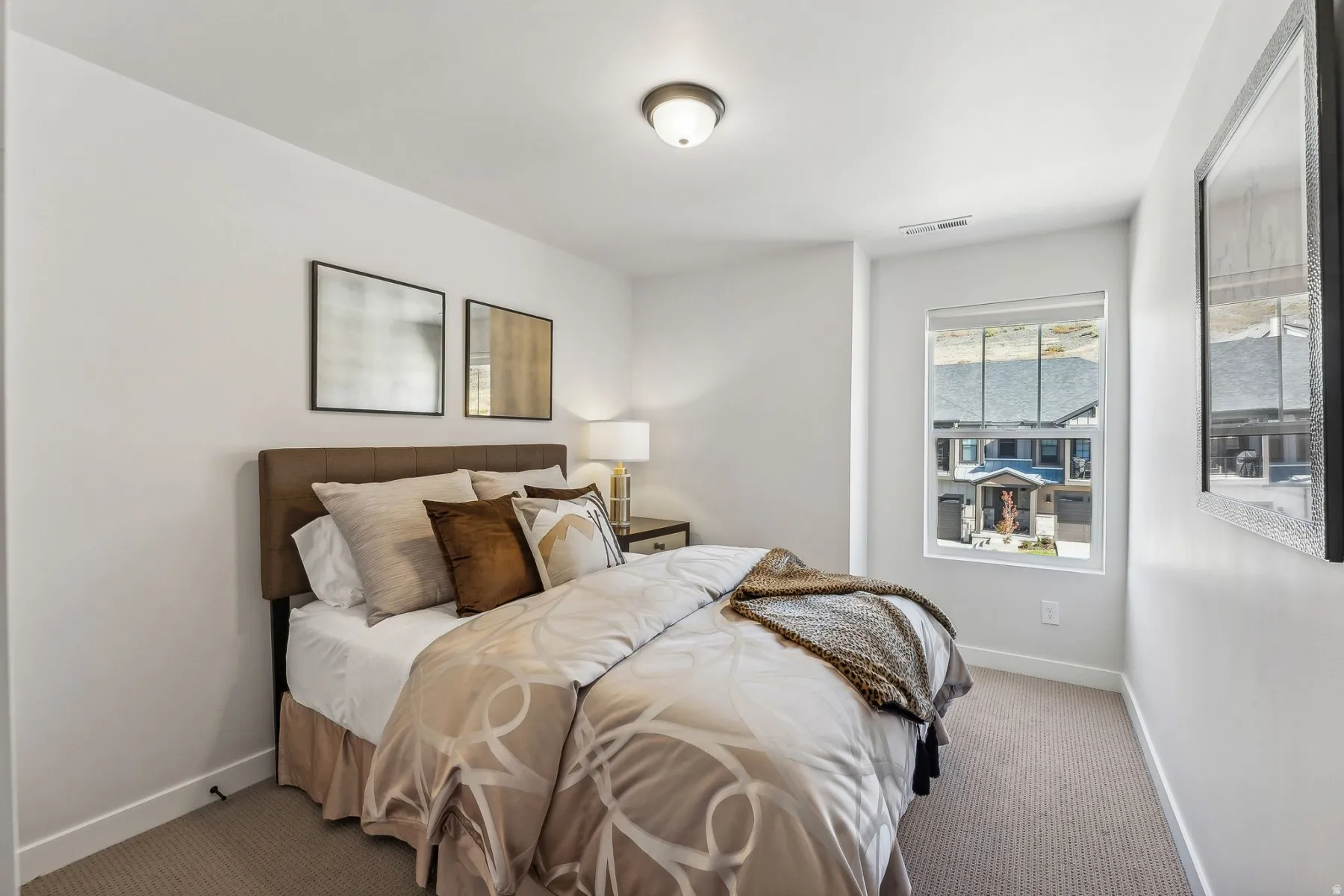 Bright secondary bedroom featuring a wood-finish bed frame, neutral bedding, layered throw pillows, and carpet flooring