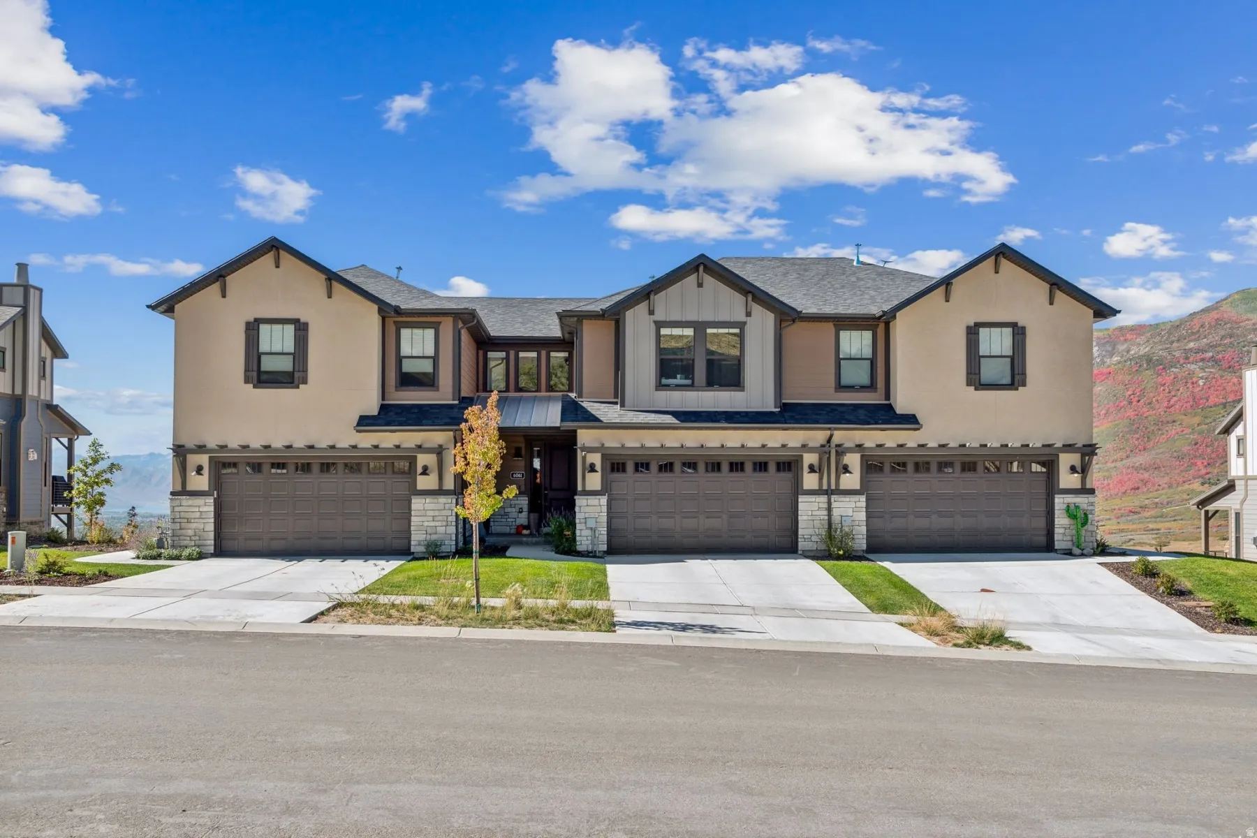 Contemporary multi-unit dwelling with stucco and wood-look siding, stone accents, and a dark shingle roof