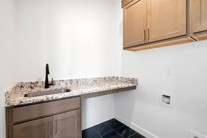 Laundry area featuring a built-in sink with a matte black faucet, speckled countertop, and dark tiled flooring