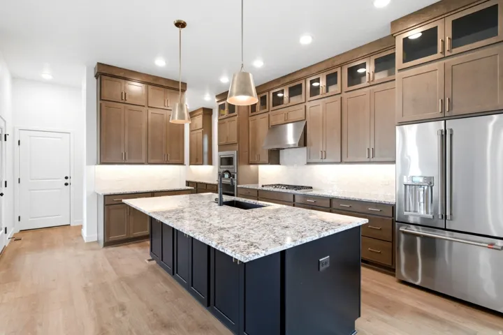 Kitchen featuring an island with ample countertop space, stainless steel appliances, wood-finish flooring, recessed lighting, and pendant fixtures