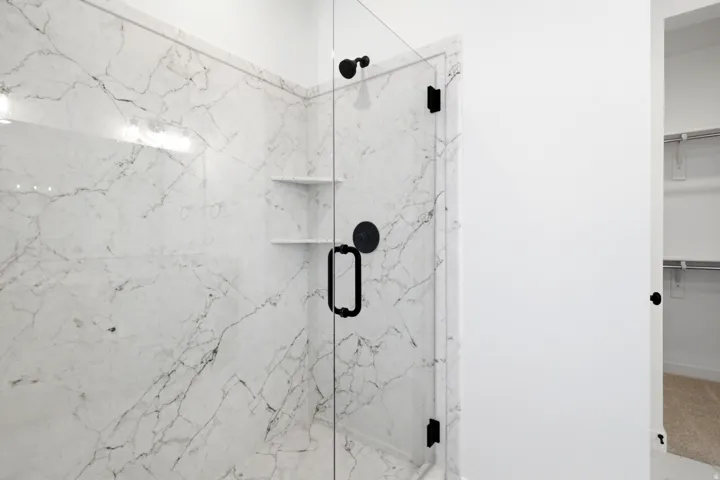 Spacious walk-in shower featuring large format marbled tile, a frameless glass enclosure, and matte black hardware