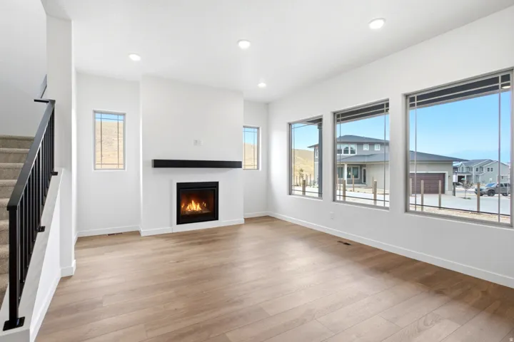 Open-concept living space featuring wood-finish flooring, a contemporary fireplace with a black mantel, and recessed ceiling lighting