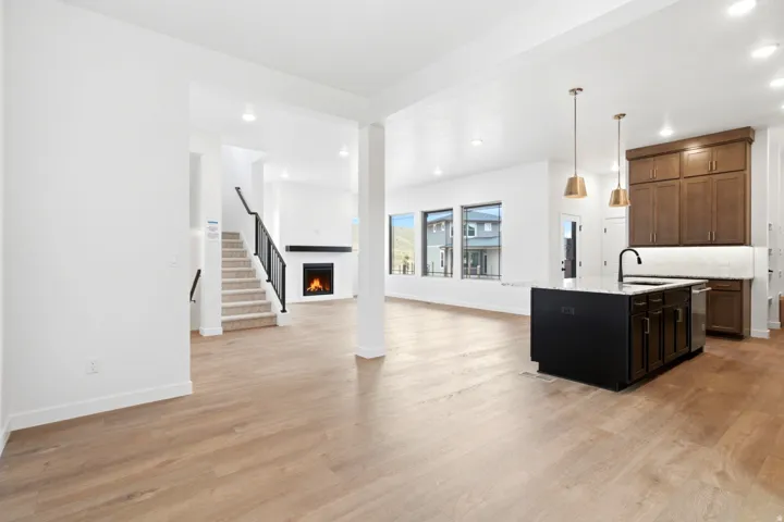 Open-concept interior featuring wood-finish flooring, a kitchen island with pendant lighting, a built-in fireplace, and a staircase with black metal railings