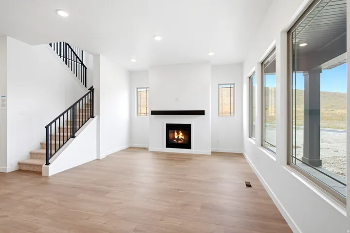 Bright living area featuring a central fireplace with a dark wood-finish mantel, recessed lighting, and expansive windows