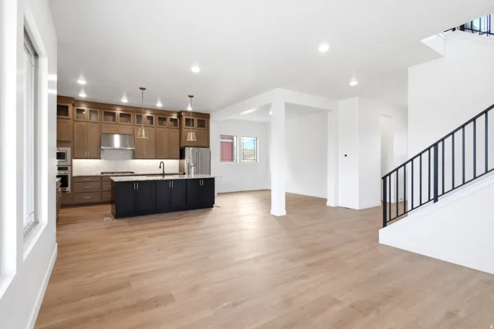 Open-concept living area featuring wood-finish flooring, a contemporary kitchen with a dark-toned island and light wood cabinetry, stainless steel appliances, and recessed lighting throughout