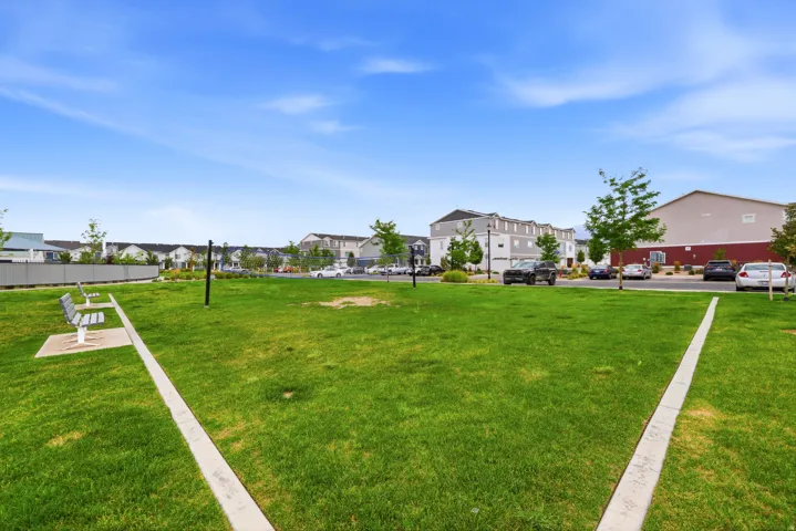 Expansive green space featuring a concrete pathway, two park benches, mature trees, and landscaping
