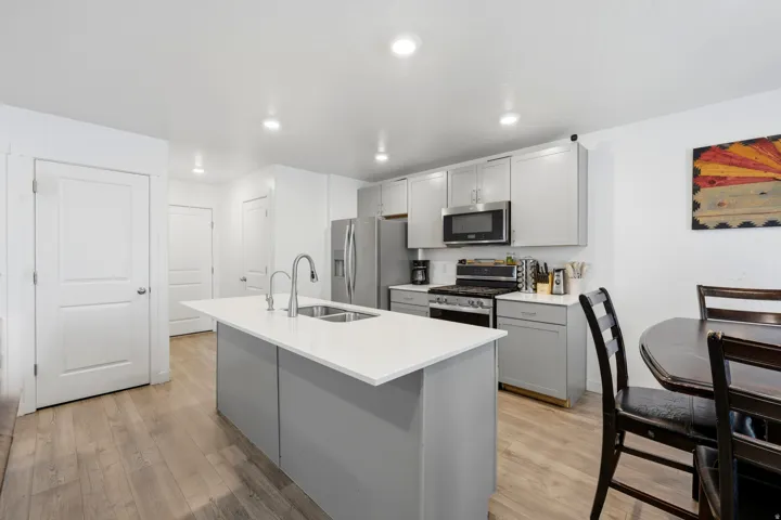 Contemporary kitchen featuring a large central island with an undermount sink and modern faucet, light gray cabinetry, stainless steel appliances, and recessed lighting