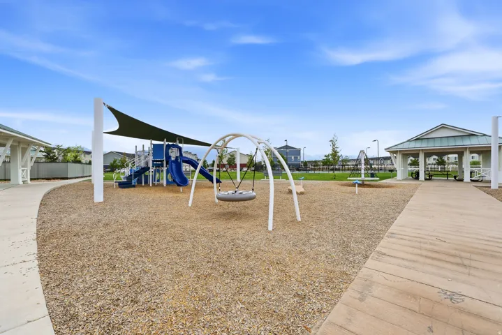 Community playground featuring a multi-level play structure with slides, swings, and a shade canopy