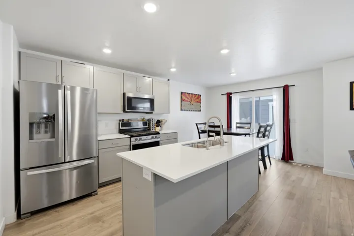 Modern kitchen featuring an island with an undermount sink, stainless steel appliances, light gray cabinetry, and recessed lighting