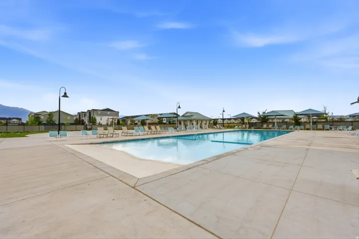 Expansive outdoor swimming pool featuring a concrete deck, multiple shade structures, and integrated streetlights