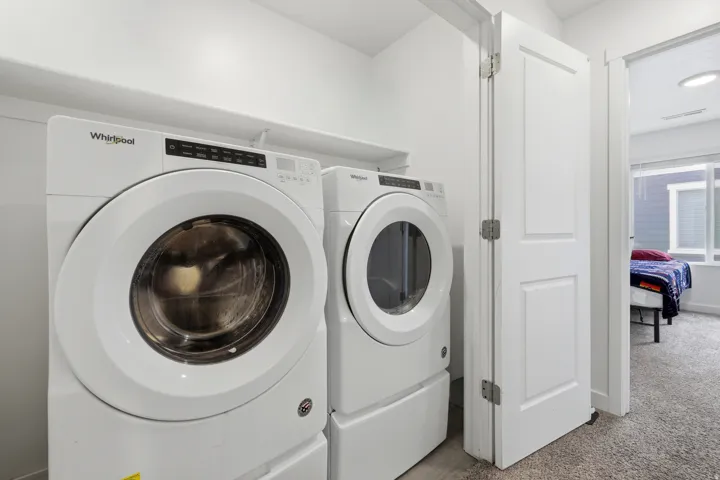 Dedicated laundry area featuring a front-load washer and dryer set, white cabinetry, and a storage shelf