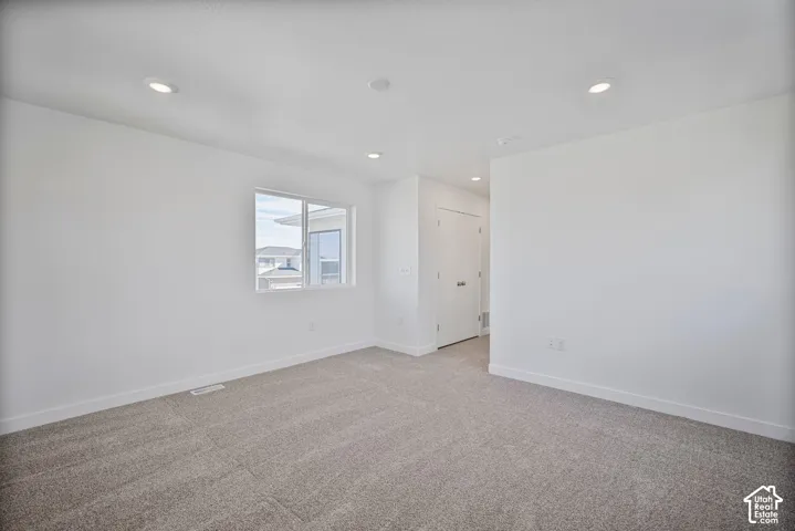 Neutral interior space featuring high-pile carpeting, smooth-finish walls, recessed ceiling lighting, a dual-pane sliding window, and a white interior door