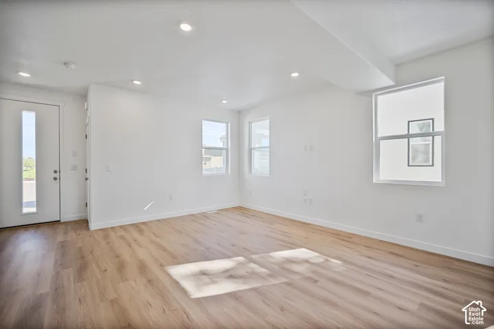 Open-concept interior featuring light-tone wood-finish flooring, recessed ceiling lighting, and a neutral white color palette