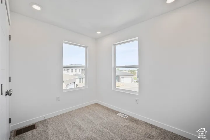 Neutral-toned interior space featuring textured wall-to-wall carpeting, recessed ceiling lighting, and dual windows with white trim