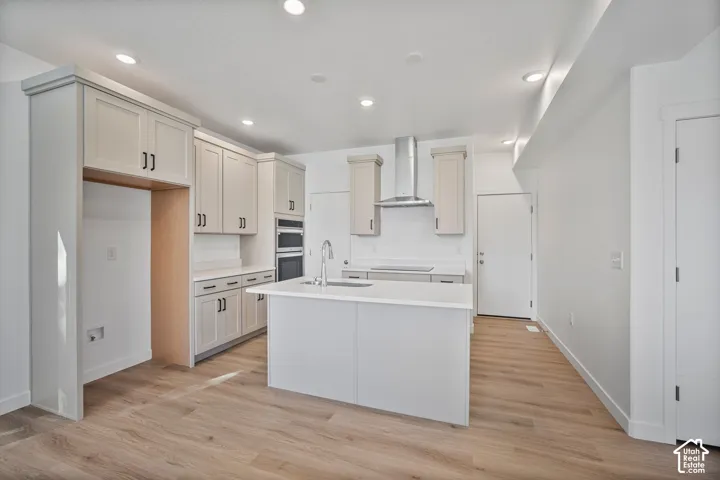 Kitchen featuring shaker-style cabinetry, quartz countertops, a center island with a stainless steel sink, built-in double wall ovens, and wood-finish flooring