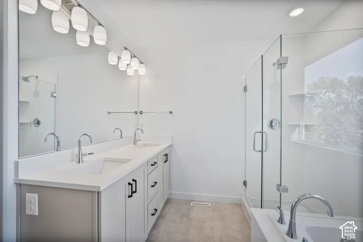 Dual-sink vanity with white cabinetry, quartz-style countertop, glass-enclosed shower, and separate soaking tub
