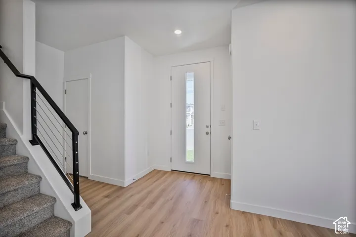 Entryway featuring wood-finish flooring, a white front door with a vertical glass panel, and a staircase with a black metal handrail and horizontal cable railing system
