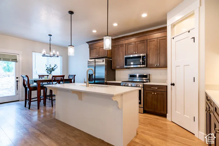 Modern kitchen featuring a central island with a sink and brass-finish faucet, stainless steel appliances, wood-finish flooring, recessed lighting, and pendant lights