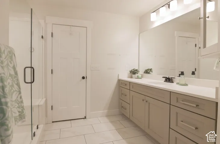 Spacious bathroom featuring a frameless glass shower enclosure with built-in bench, light-toned floor tile, an expansive vanity with a light countertop, integrated sink, and modern cabinetry with brushed nickel hardware, illuminated by a multi-bulb vanity