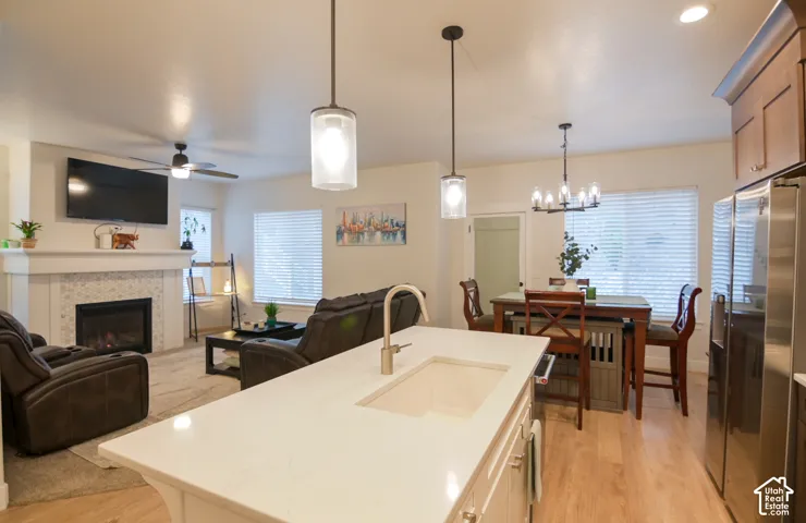 Open-concept living space featuring a fireplace with a tile surround, a built-in ceiling fan, wood-finish flooring, a kitchen island with a built-in sink, and stainless steel appliances