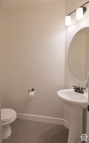 Pedestal sink with dark bronze faucet, circular mirror, and two-light vanity fixture