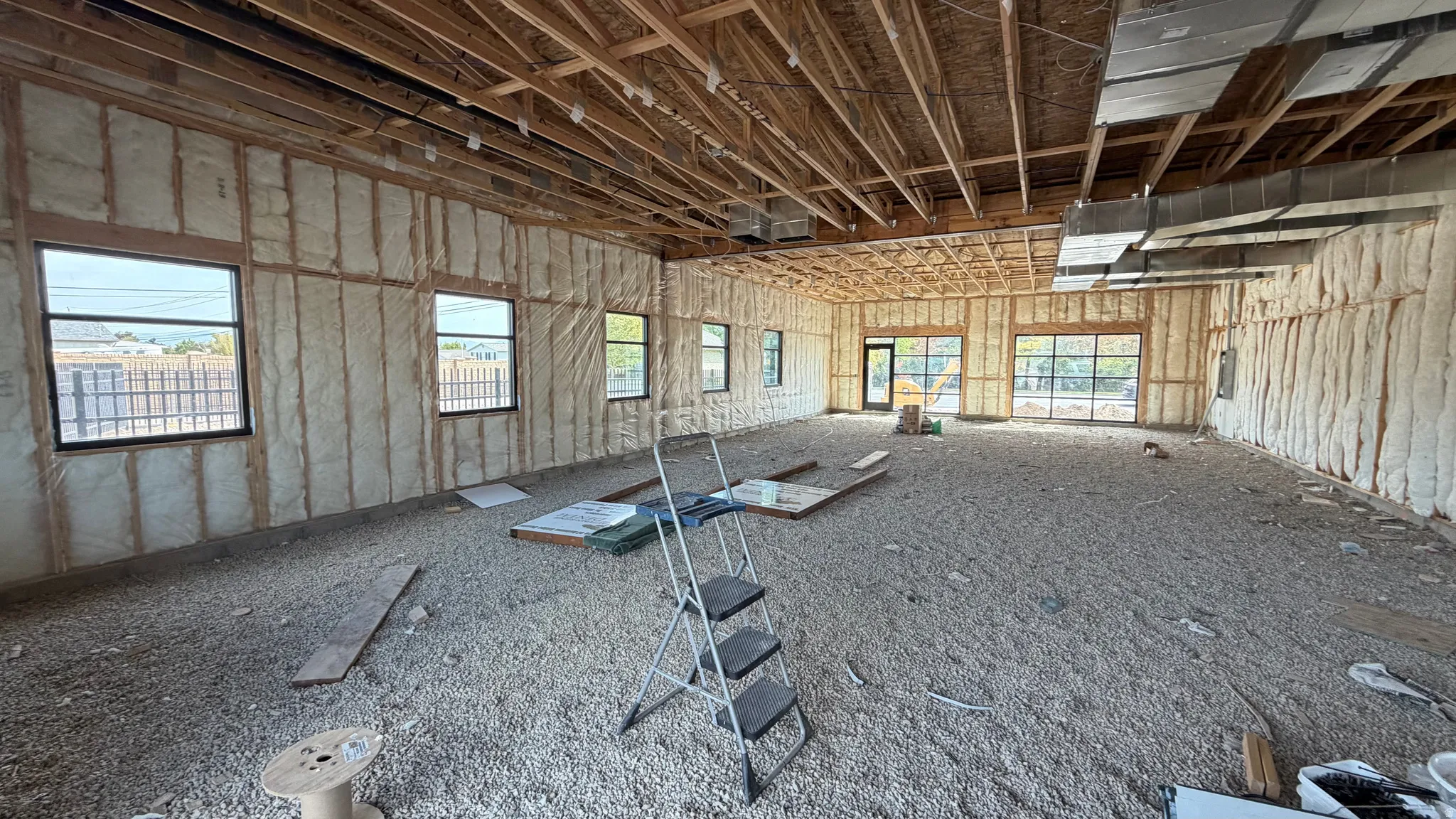 Open-concept interior featuring exposed ceiling joists, spray foam insulation, multiple black-framed windows, and a large glass-paned door