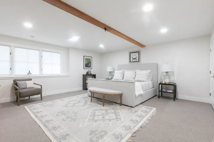 Spacious room featuring neutral carpeting, white walls, and a prominent wood ceiling beam