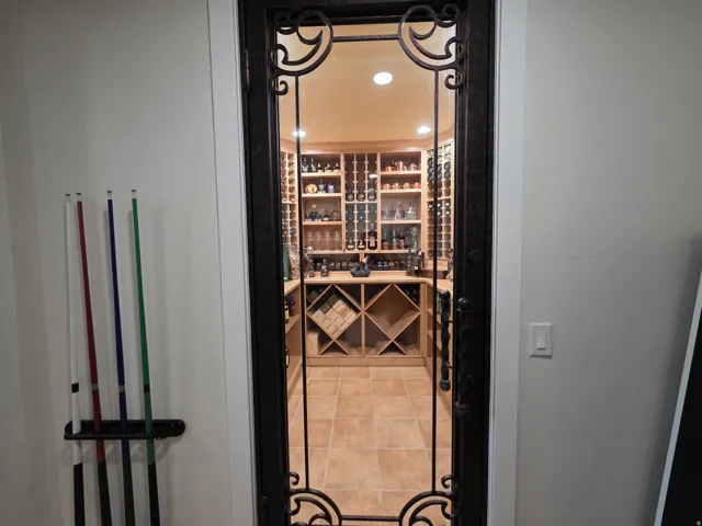 Wrought iron and glass entry door leading to a dedicated wine cellar featuring extensive wood-finish shelving, built-in bottle racks, and tile flooring